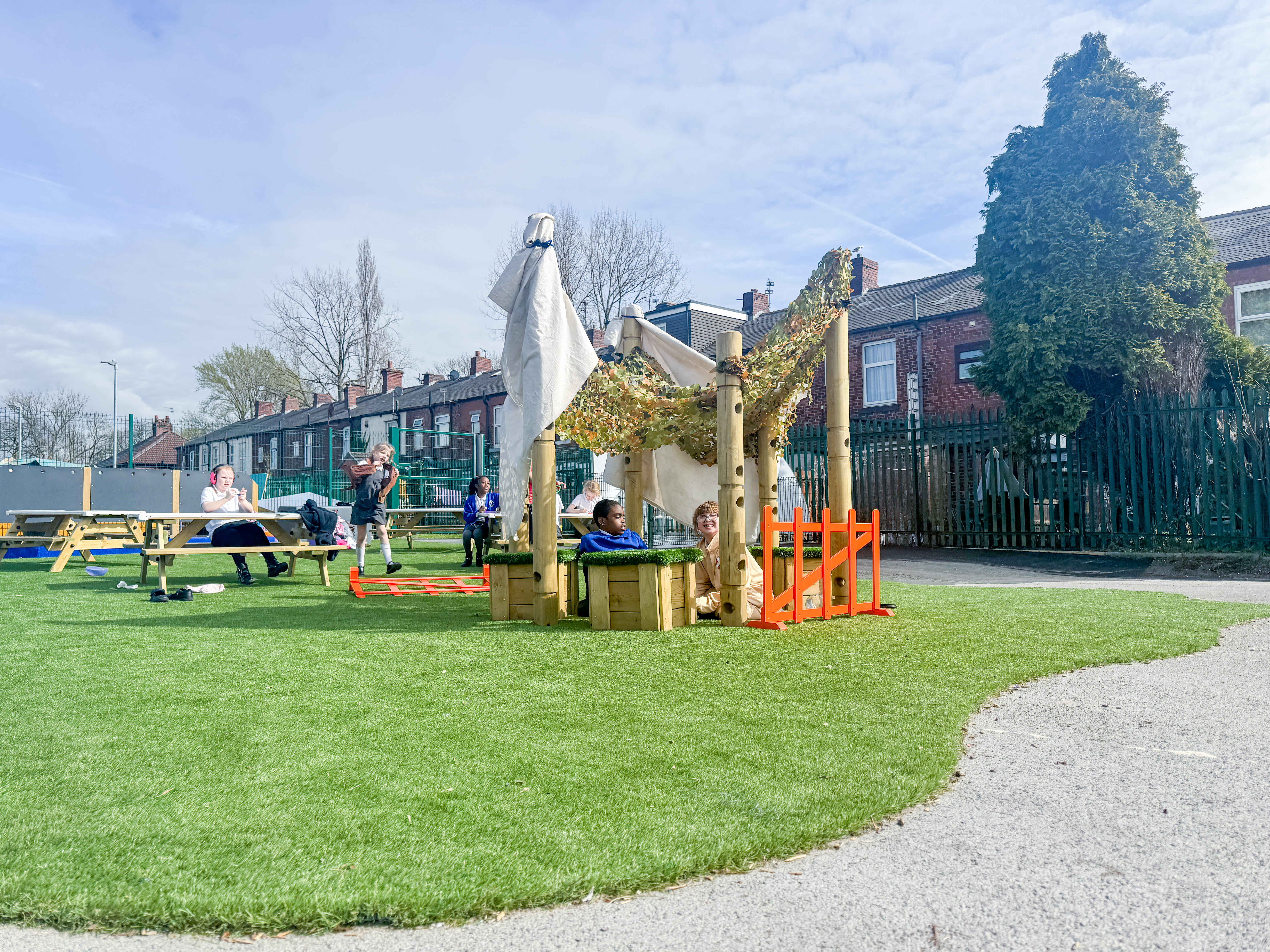 A small group of children are stood underneath a den, that has been constructed by tying fabric to the Den Making Posts.