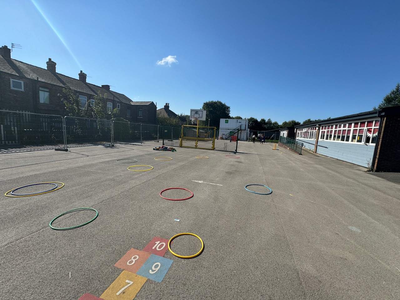 An old tarmac playground with hoolahoops scattered across the surfacing, with faded thermoplastic markings.