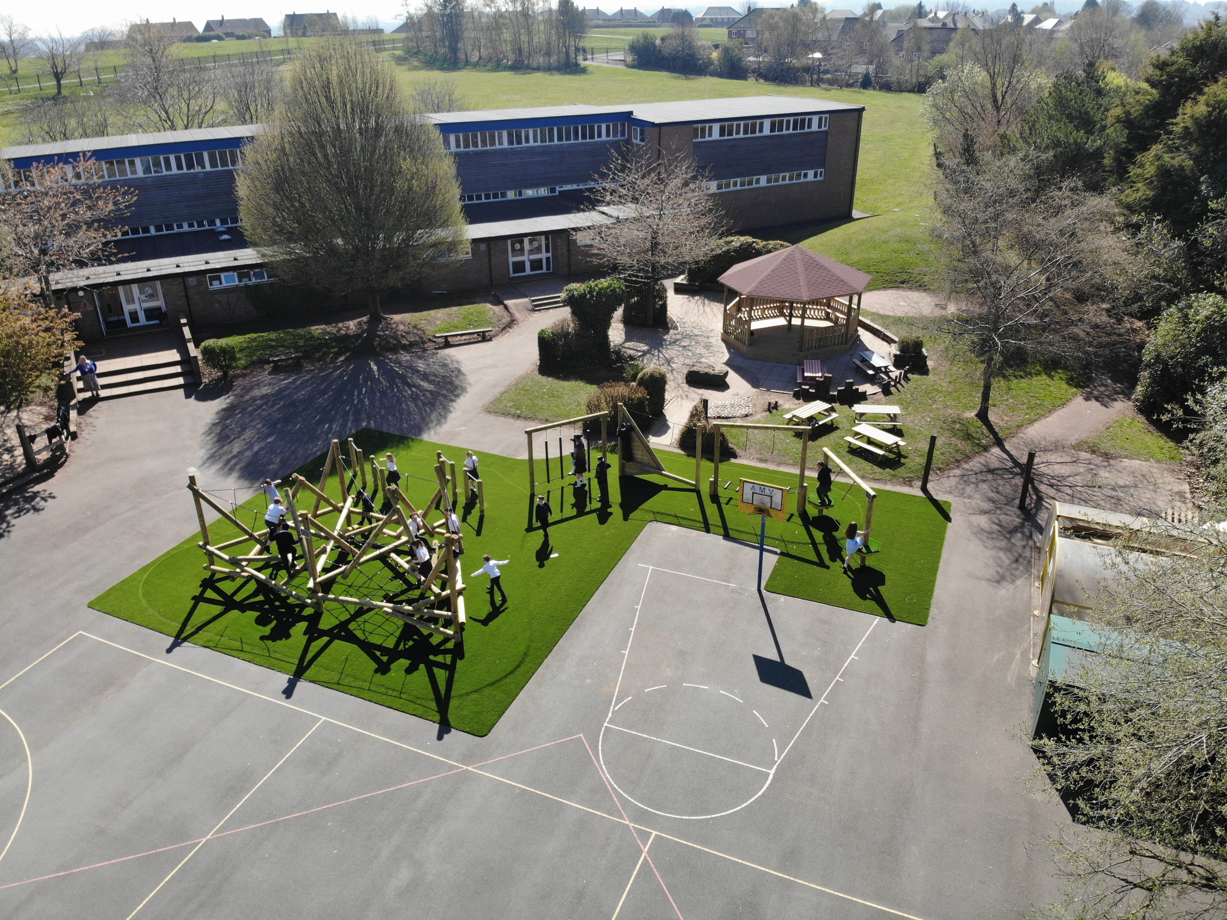 A drone shot which showcases the Helm Crag Climber on artificial grass, and the bespoke forest trim trail on the Weston Junior Academy playground.