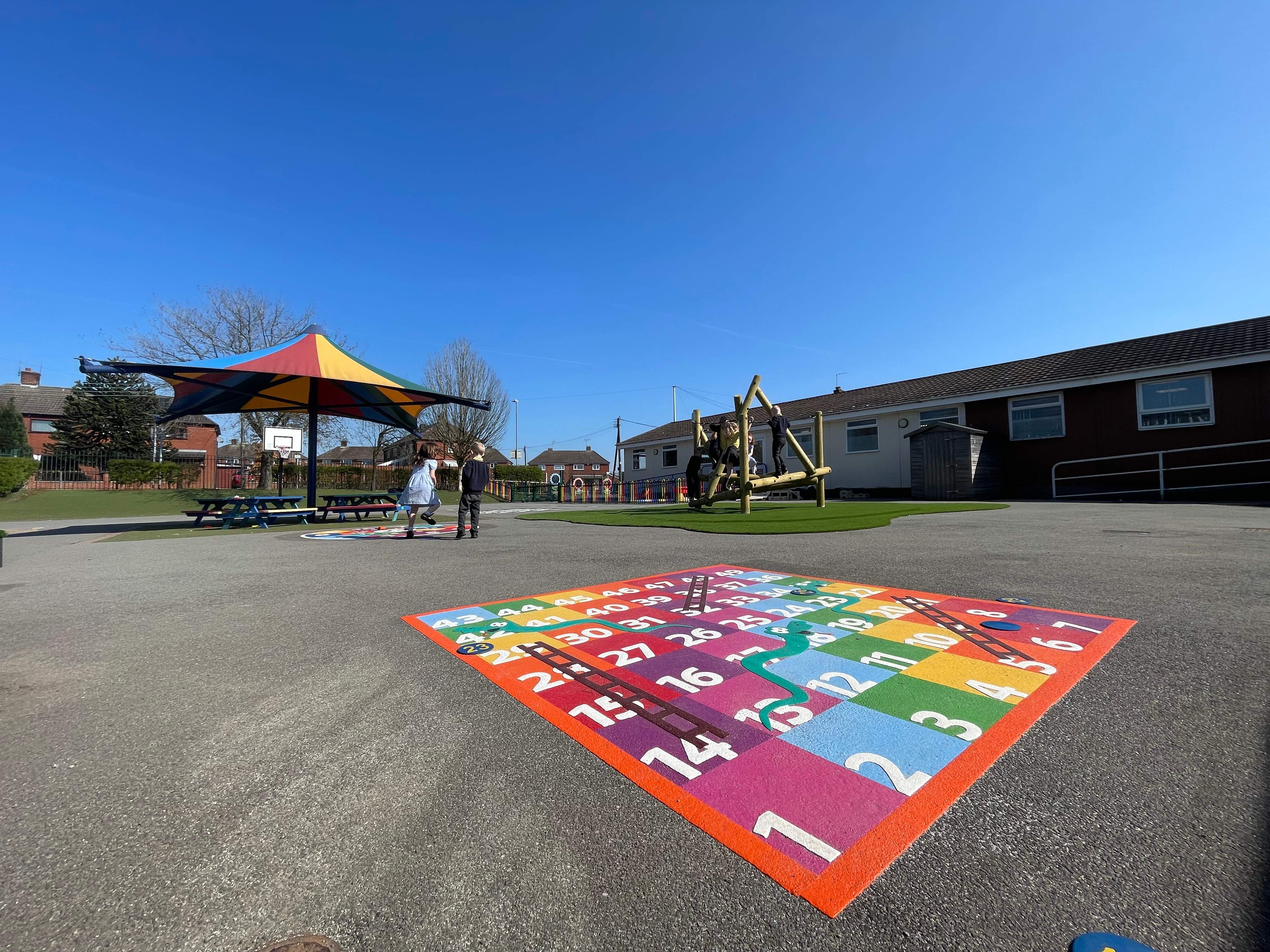 A close up of the thermoplastic markings, with a shelter on the playground. Children are running around the playground.