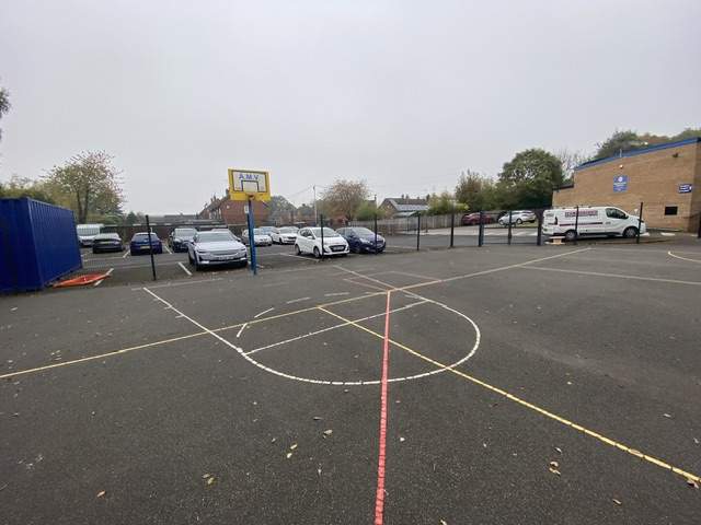 A worn-down tarmac playground with broken thermoplastic markings scattered around.