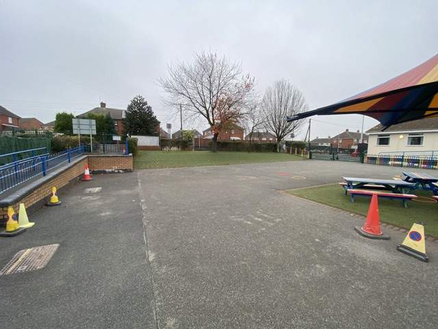 An old tarmac playground with cones scattered around covering pot holes.