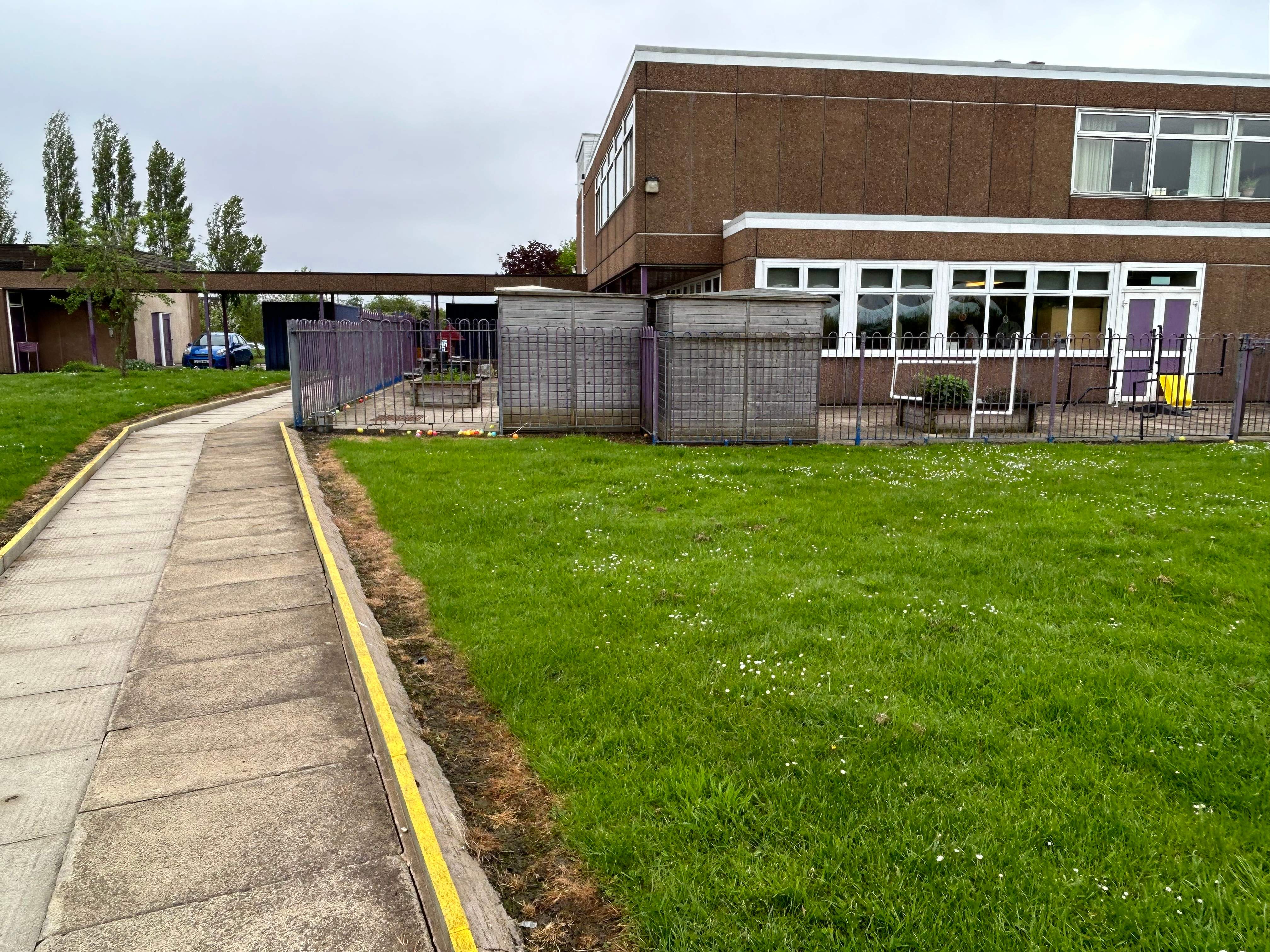 A concrete pathway beside an area of natural grass with a border of dead grass.