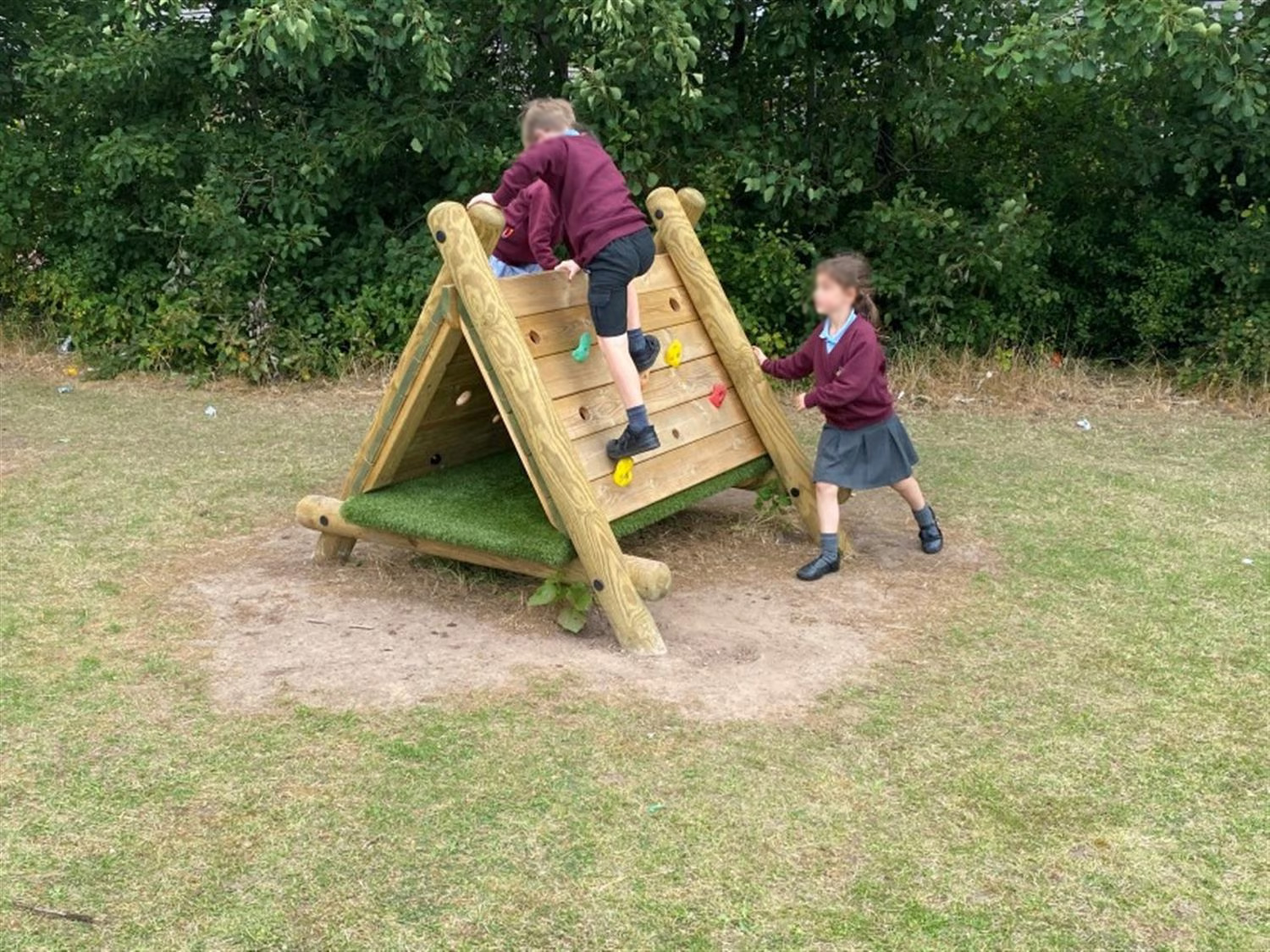 two children climb over the climbing wall exterior of the triangle tunnel