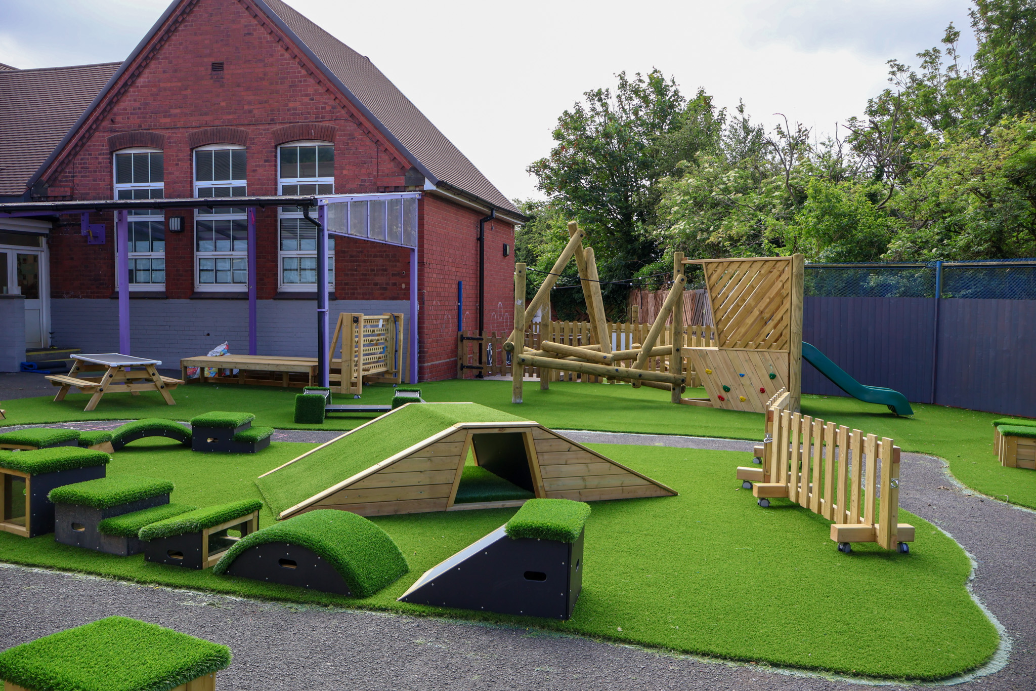 An active play area that has been installed on an artificial grass surface with loads of freestanding and installed play equipment.