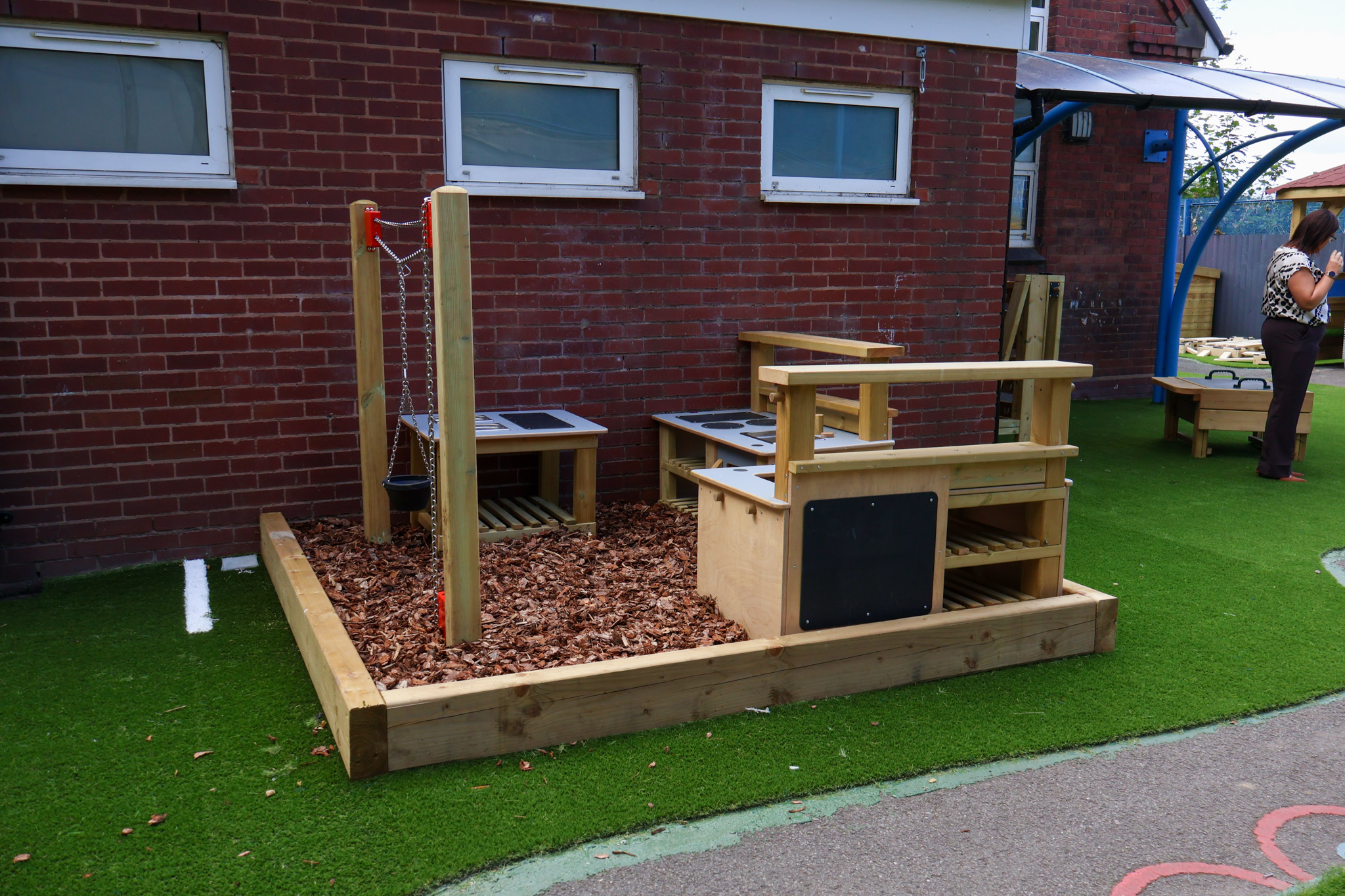 A messy play area located within a wooden bark chip surfaced space, with mud kitchens and a chain and pulley.