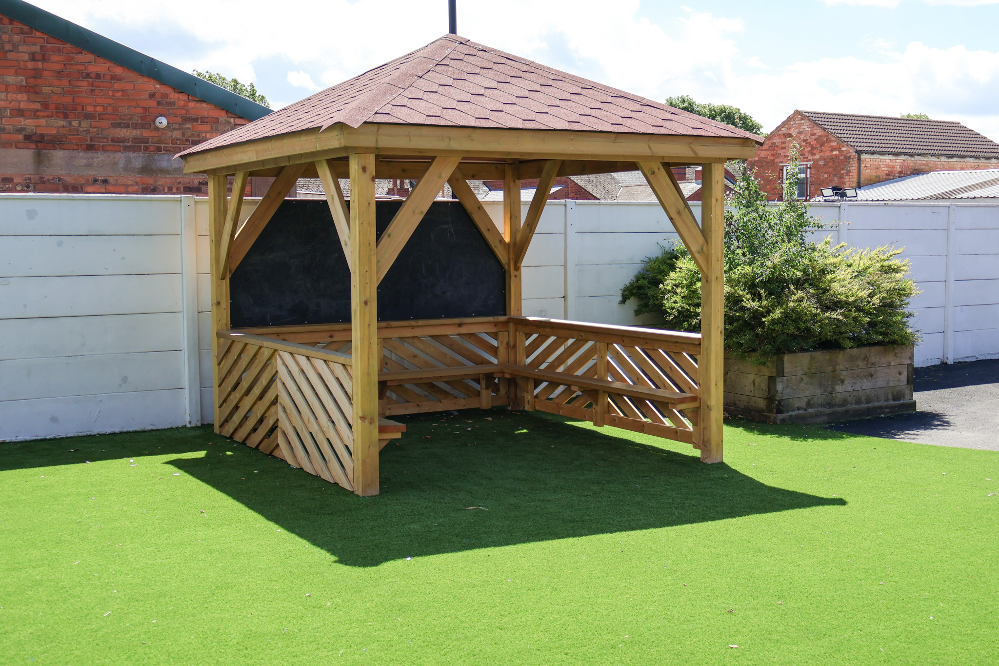 A 3M square gazebo with a chalkboard and bench, installed on top of artificial grass.