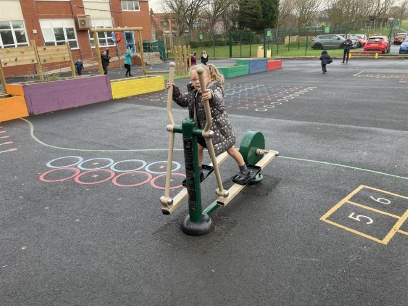 A girl in a coat using a green steel elliptical cross trainer in their school playground