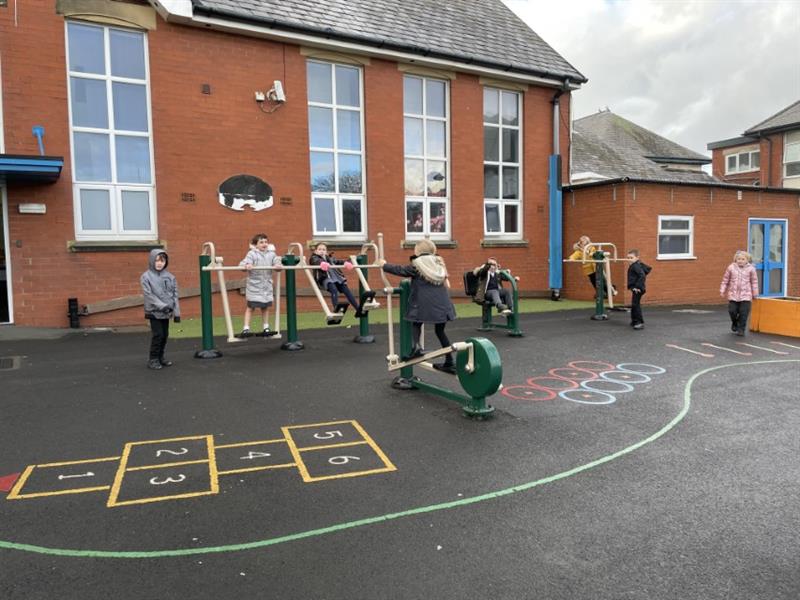 7 children in coats playing on green steel outdoor gym equipment installed onto their school playground