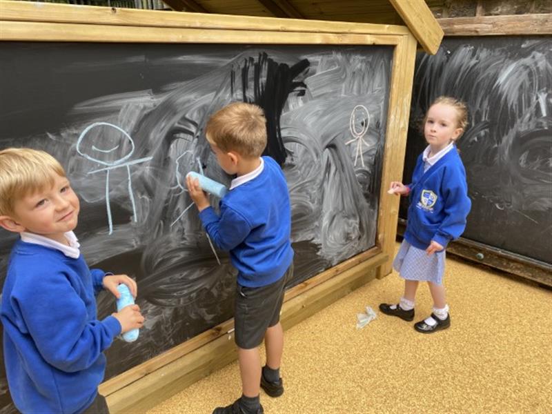 3 children drawing on the back chalkboard of a giant playhouse