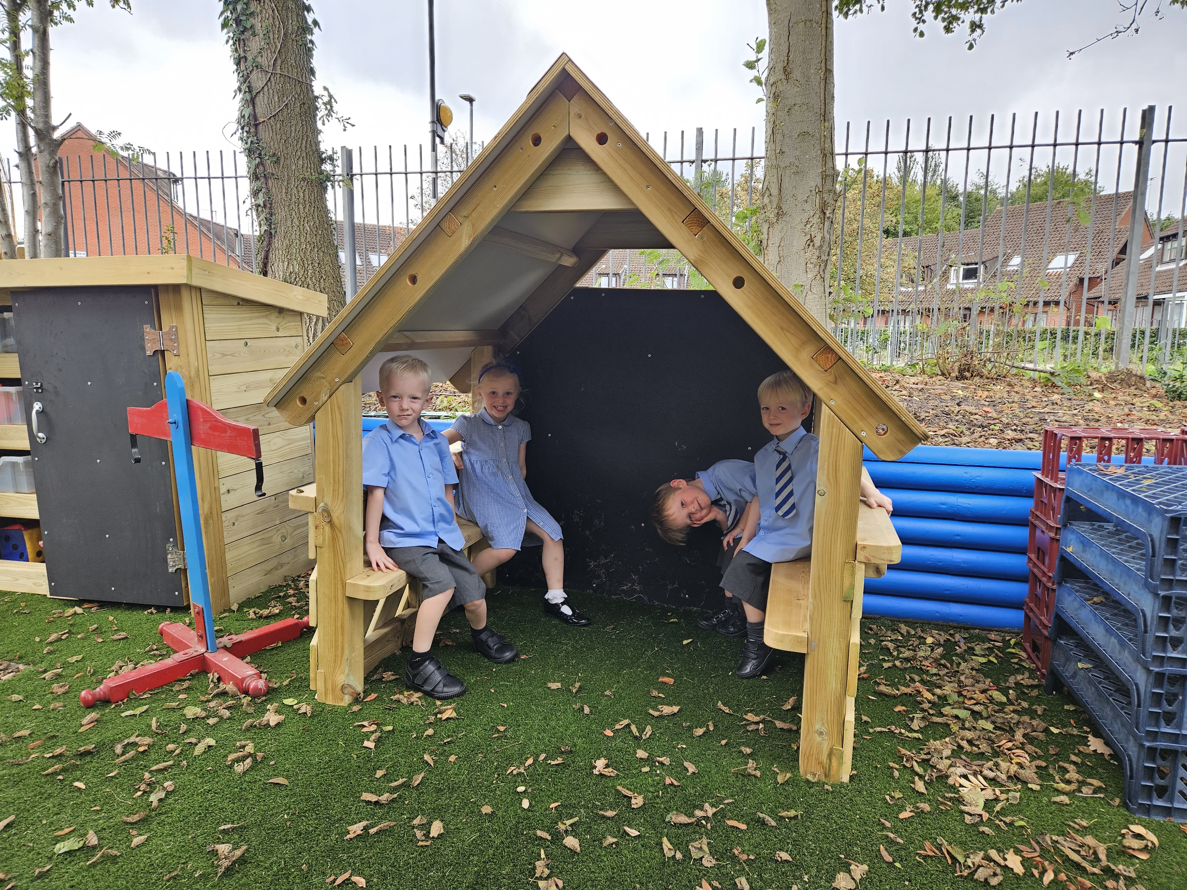 4 children are sat inside the Pentagon Small Playhouse as they look at the camera, smiling. The small playhouse allows the children to play and have fun.
