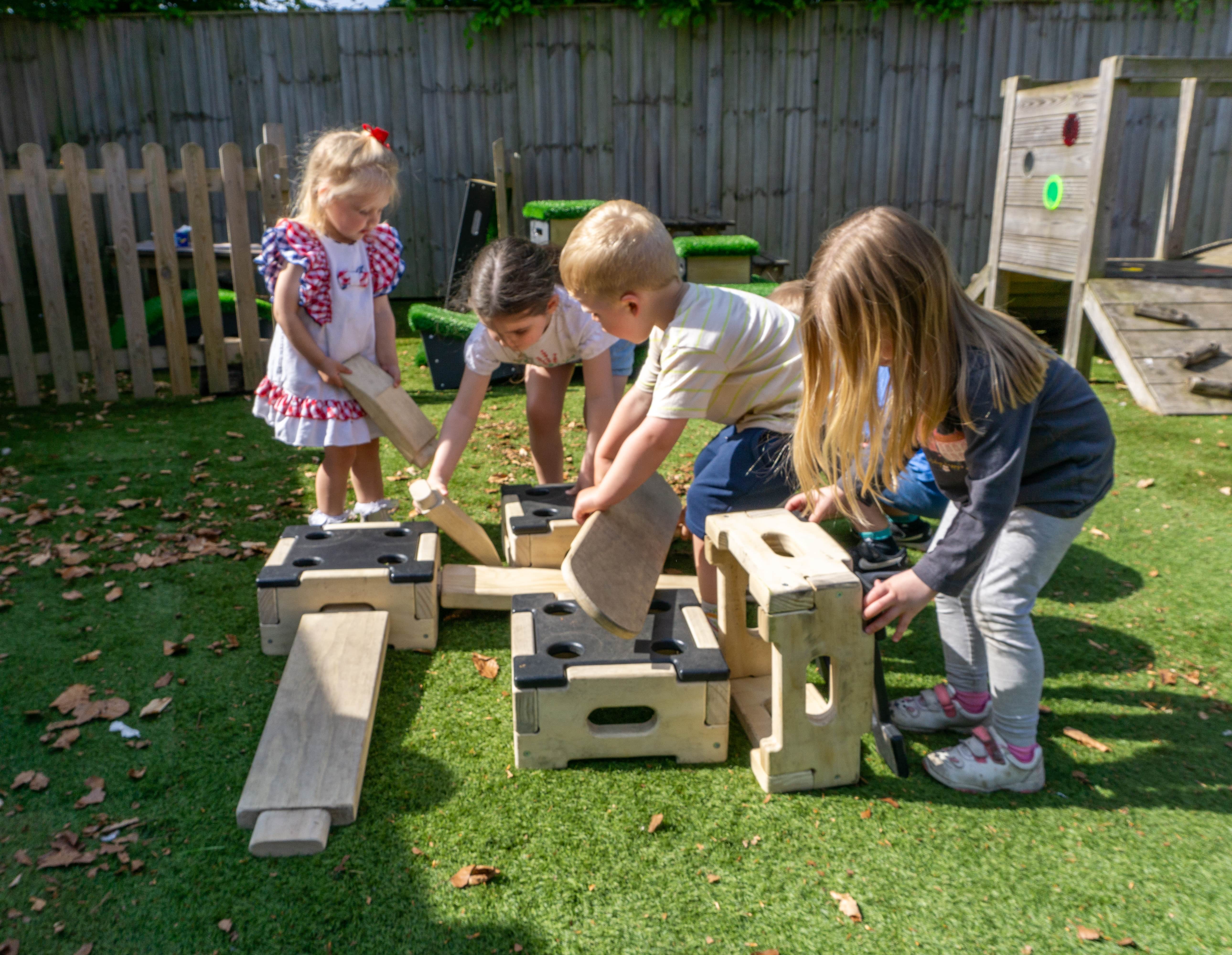 A group of four children are moving the parts of the Play Builder Set that Kindred White Post bought. This Play Builder Set is the Engineer one. The children are all grouped together, picking up different planks and blocks.