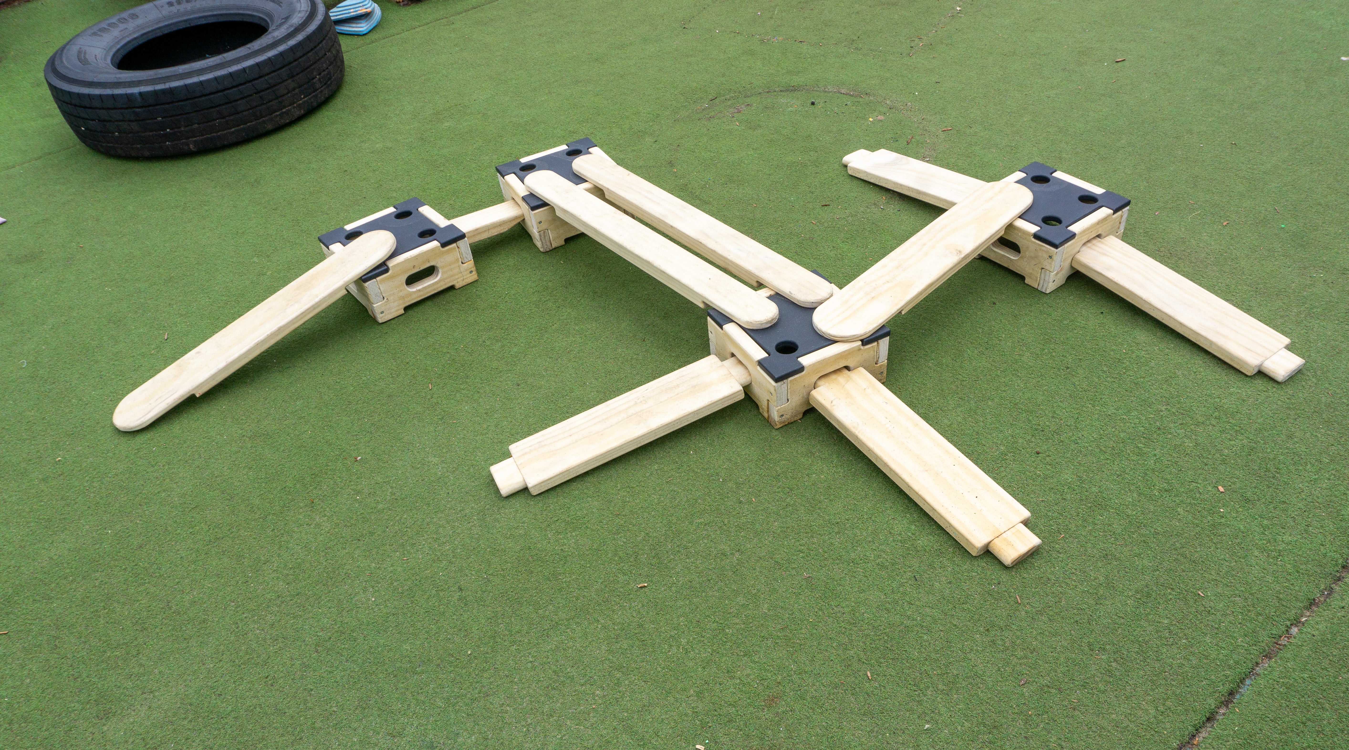 The Play Builder Apprentice set laid on top of artificial grass. 9 planks and 4 blocks can be see on the photo as they connect to form a random shape.