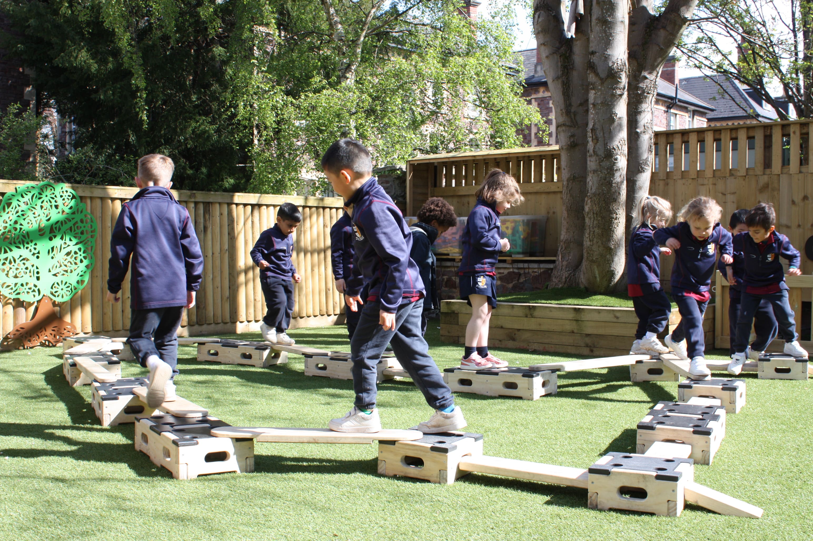 A group of children are walking around on the Play Builder Engineer Set, trying to complete the obstacle course they have created. The set is made up from wooden planks and wooden blocks.