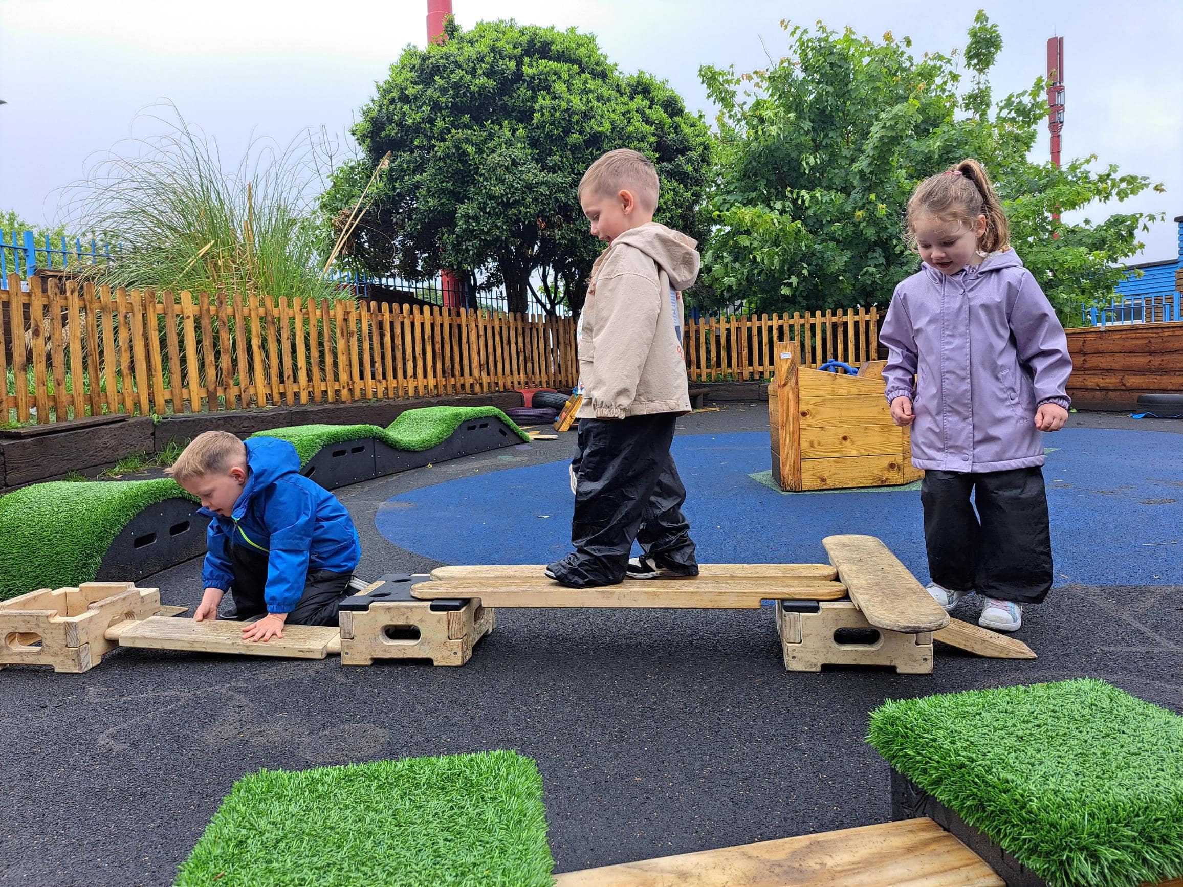 2 children are walking across a wooden plank which is connected to two wooden blocks. One child is on the floor and is connecting another wooden plank to a block to create a bridge.