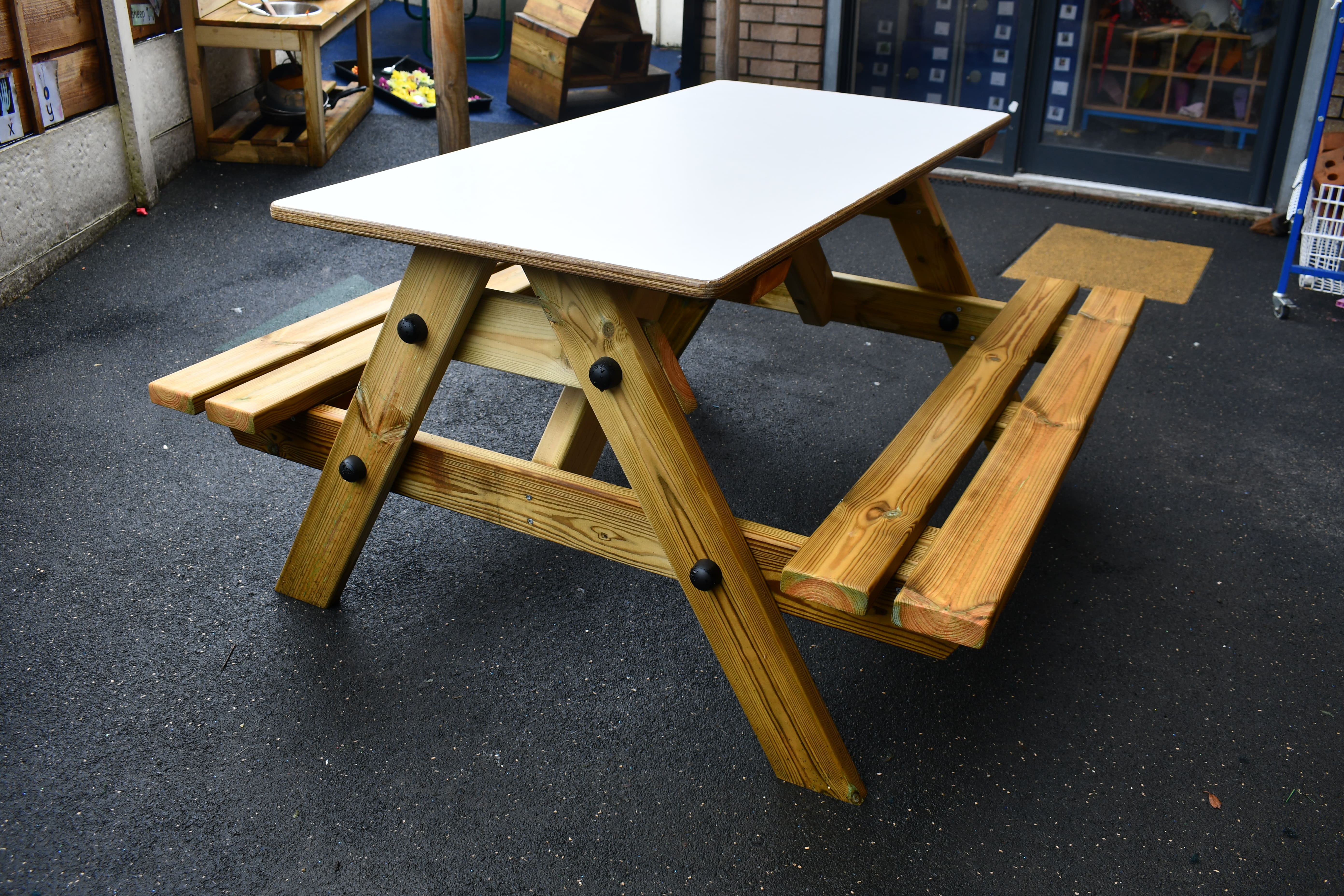 The EYFS Picnic Table. It has a white tabletop with natural wood colouring everywhere else. The Early Years Picnic Table can seat up to 4 children.