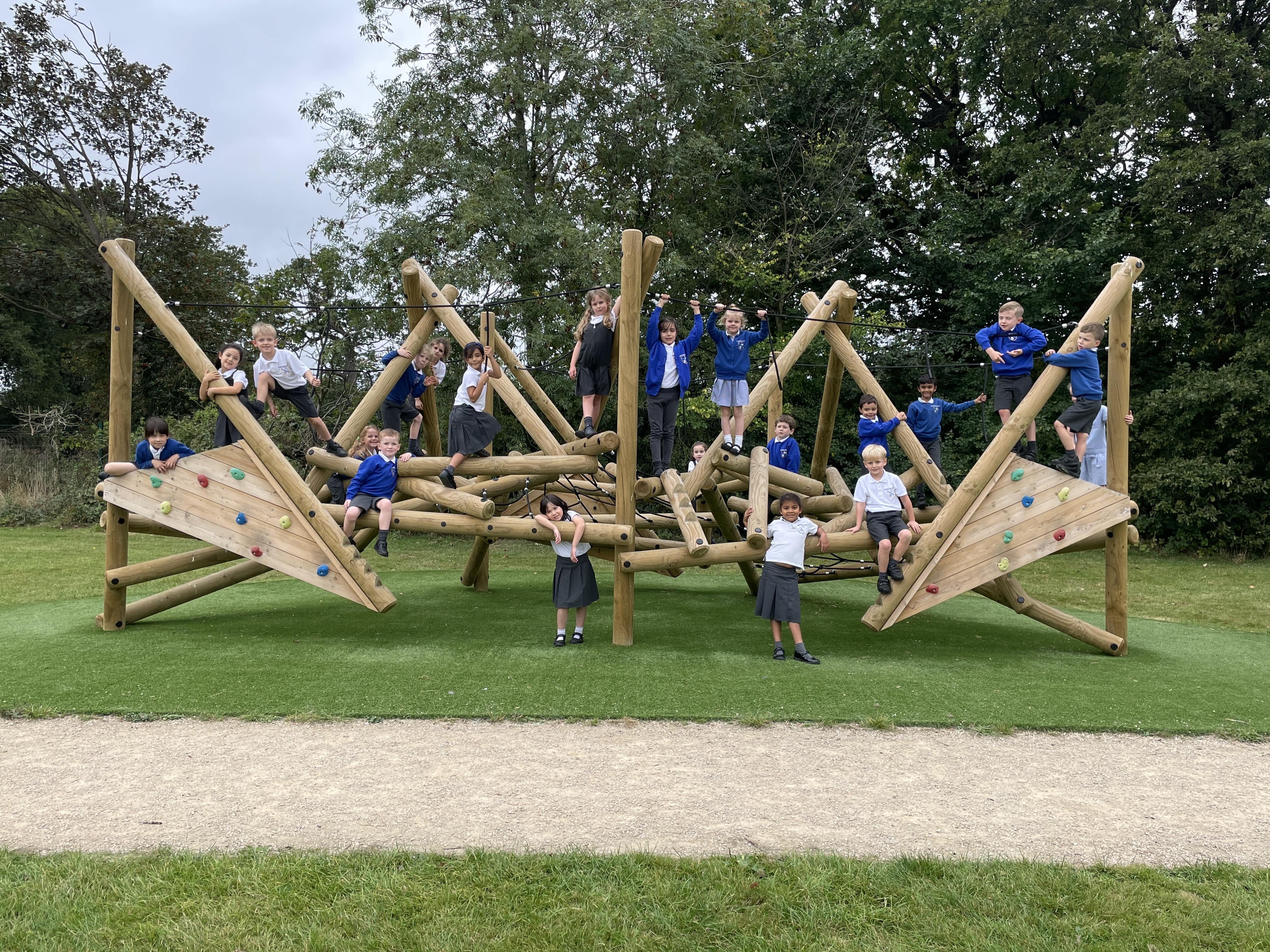 A photo showcasing the Crinkle Crags climber with a class of children all playing on the wooden climbing frame. It's been installed on an artificial grass surface.