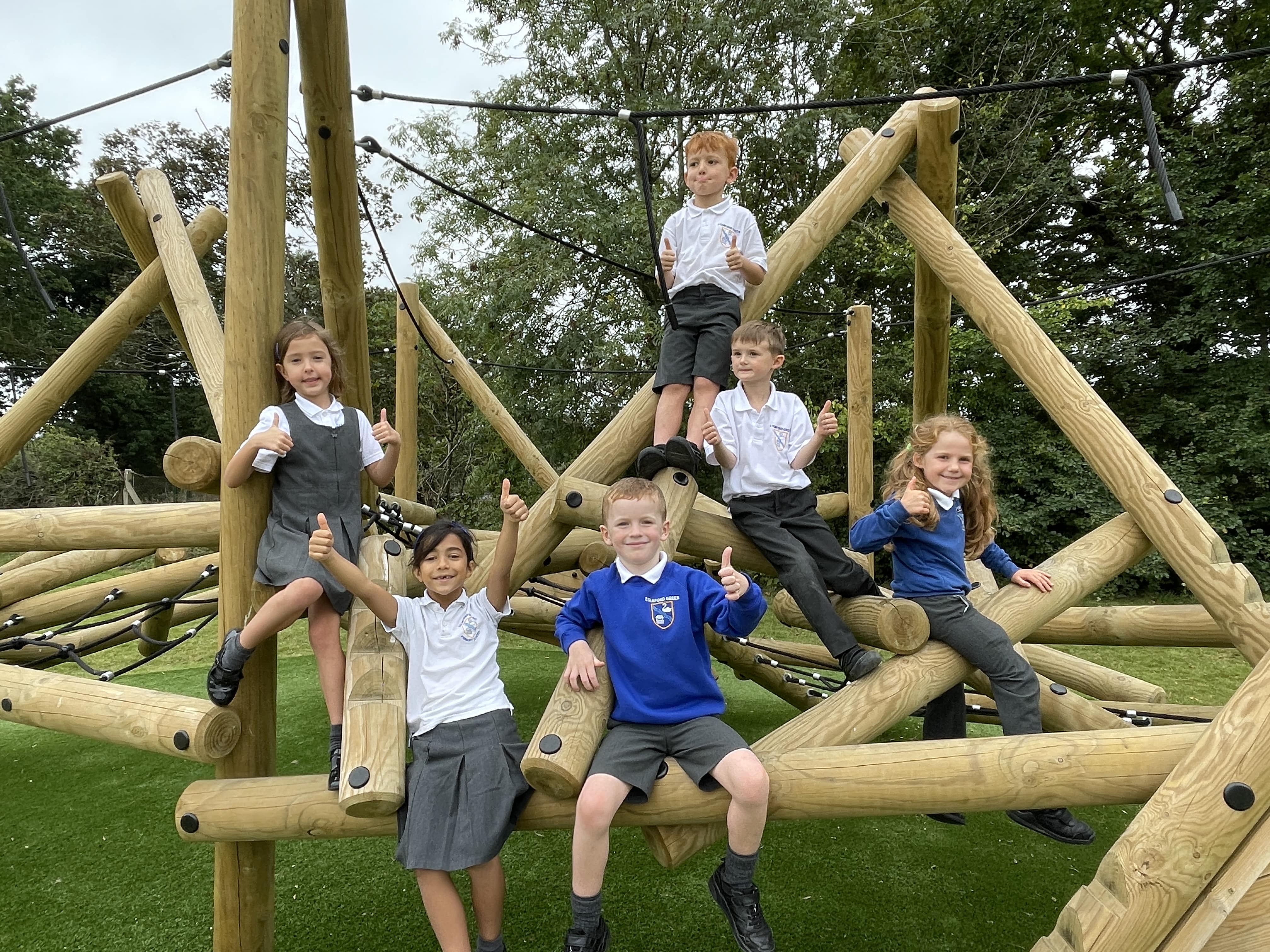 A group of children are sat on the poles of the Crinkle Crag and are putting their thumbs up and smiling at the camera.